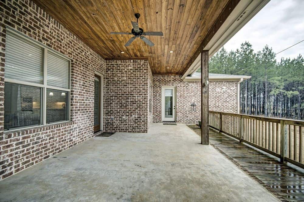 The covered porch includes wooden posts and a wood-paneled ceiling mounted with a fan.