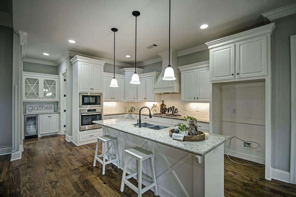 The kitchen offers white cabinetry, granite countertops, and a breakfast island paired with white bar stools.
