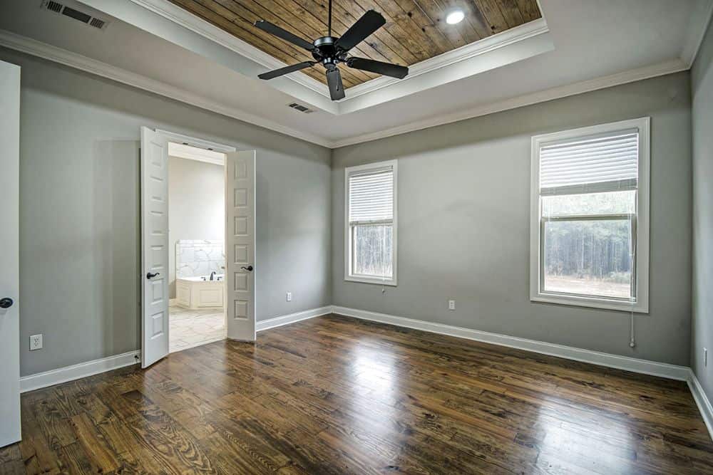 Primary bedroom with hardwood flooring, tray ceiling, and a white double door leading to the primary bath.