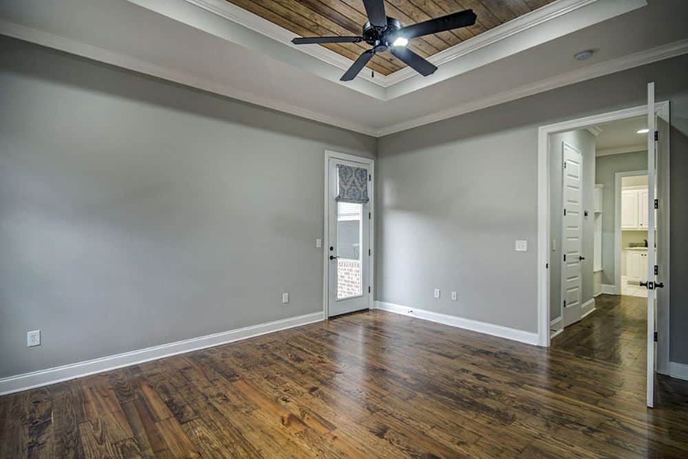 Primary bedroom with hardwood flooring, tray ceiling, and a white double door leading to the primary bath.