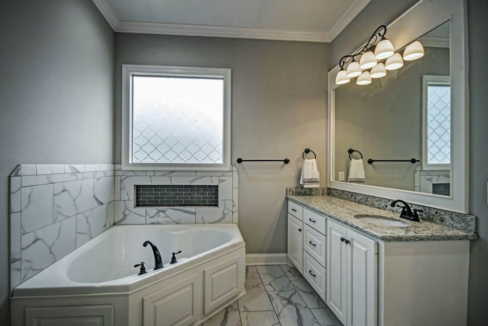 Primary bathroom with a sink vanity and a corner bathtub accentuated with a marble backsplash.