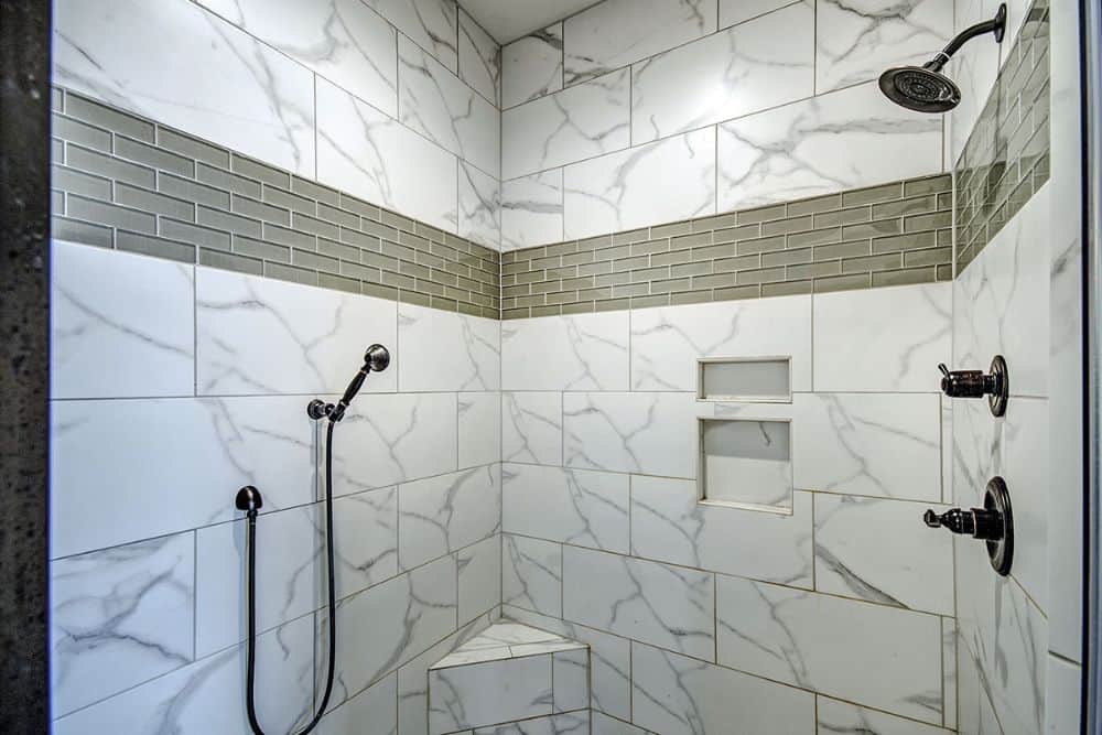 The walk-in shower has marble tiled walls, wrought iron fixtures, inset shelves, and a corner seat.
