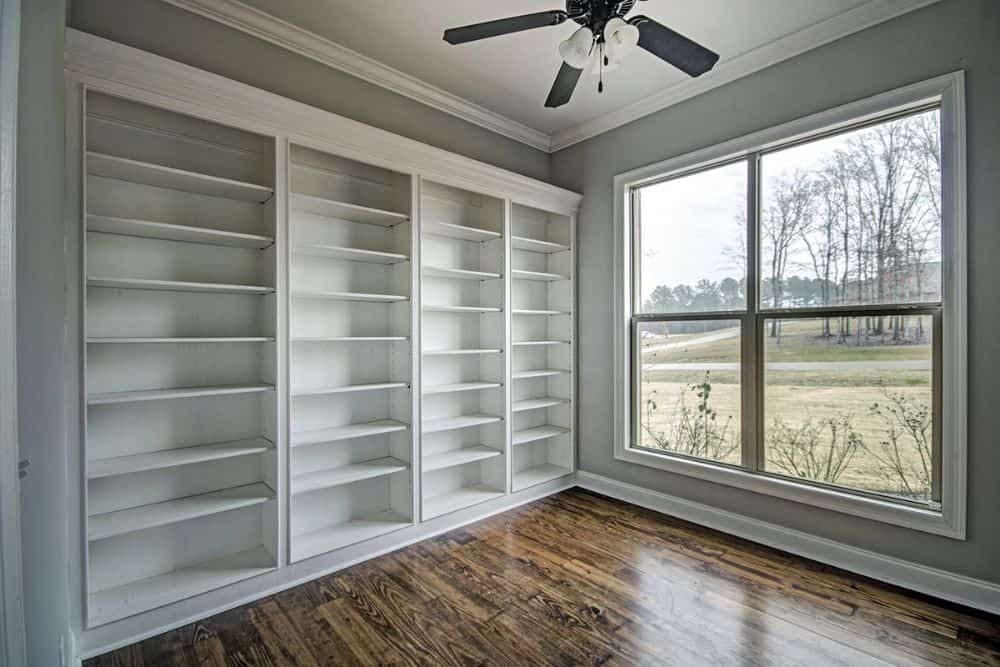 Home office with white built-in shelves and a large window overlooking the serene surrounding.