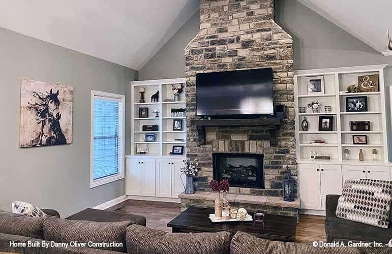 Living room with cozy seats, a dark wood coffee table, and a stone fireplace flanked by white built-ins.