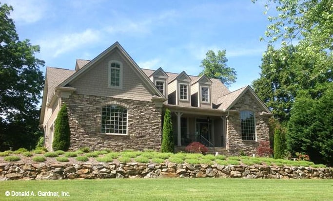 Front exterior view showing the stone cladding and a covered porch topped with three gable dormers.