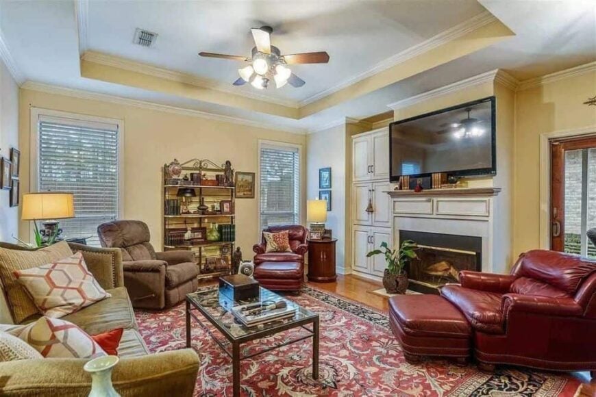 The family room has a tray ceiling, leather and fabric seats, and a fireplace topped with a TV.