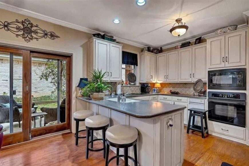 Kitchen with white cabinetry, a double wall oven, a breakfast bar, and sliding glass doors that open onto a concrete patio.