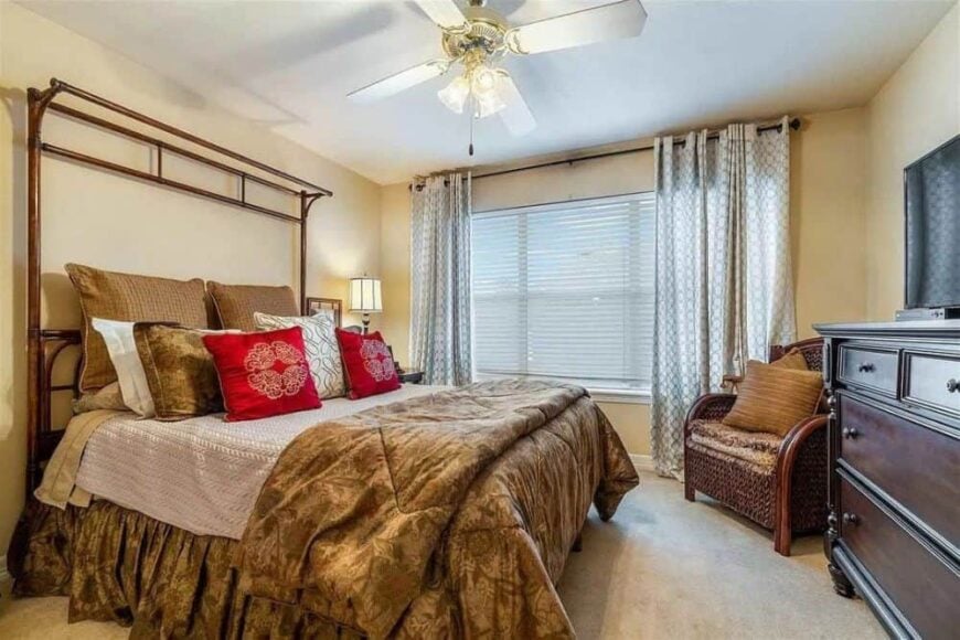 Primary bedroom with a cozy wooden bed and a wicker armchair over carpet flooring.