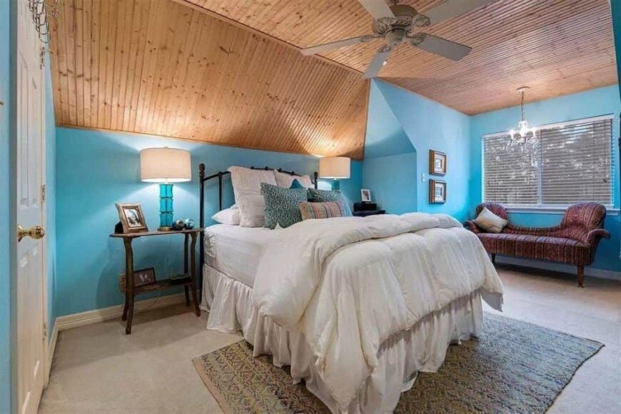 Blue bedroom with carpet flooring, a patterned chaise lounge, and a vaulted ceiling clad in wood planks.