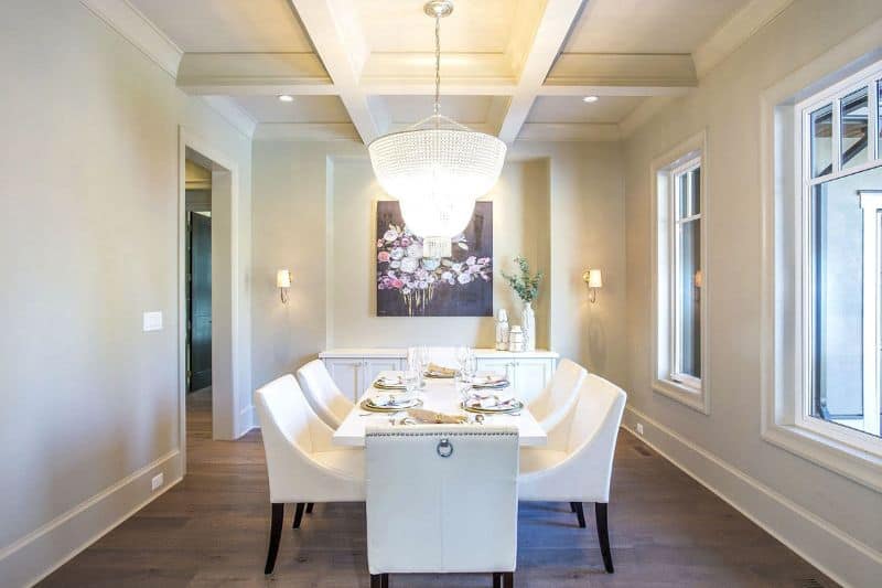 Formal dining room with a white buffet table and matching dining set well-lit by a beaded chandelier that hangs from the coffered ceiling.