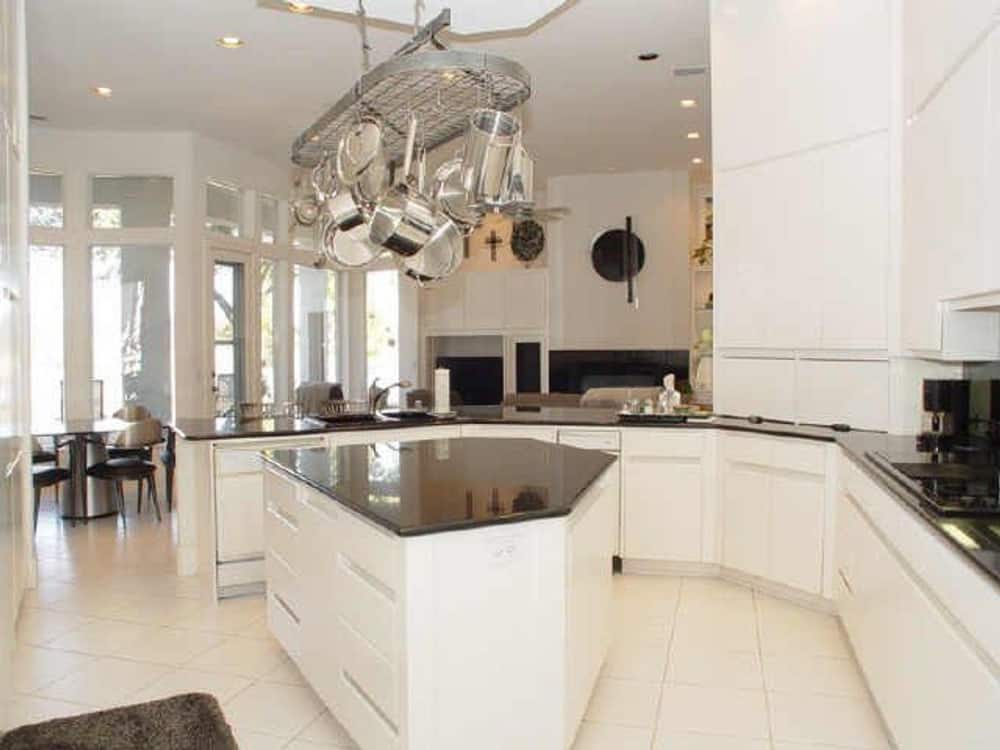 Kitchen with white cabinetry, black granite countertops, and a stainless steel pot rack suspended above the center island.