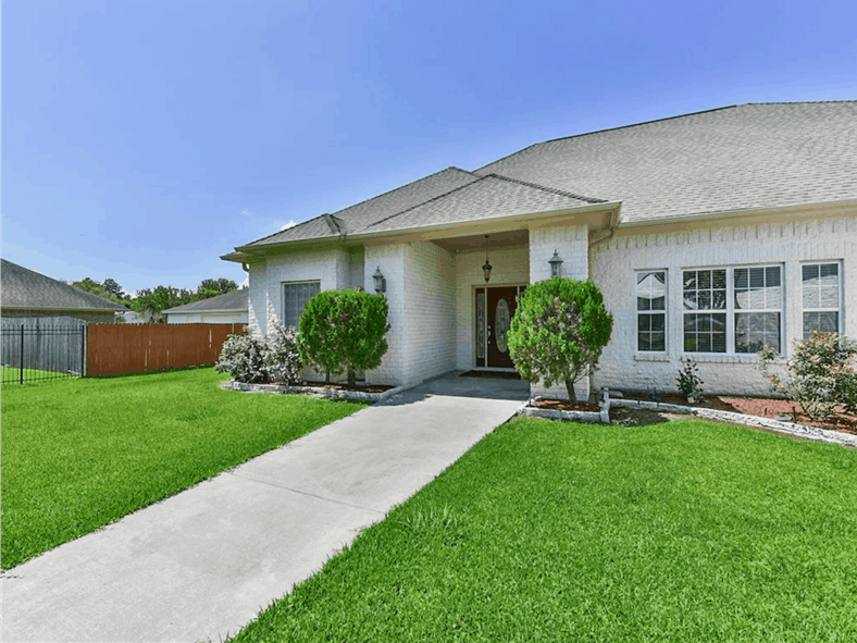 Home entry with a glazed front door and a concrete walkway nestled between the lush green lawn and plants.