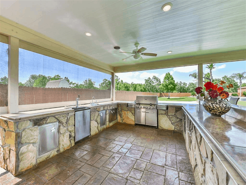 Outdoor kitchen with a built-in grill, a sink, and stone counters.