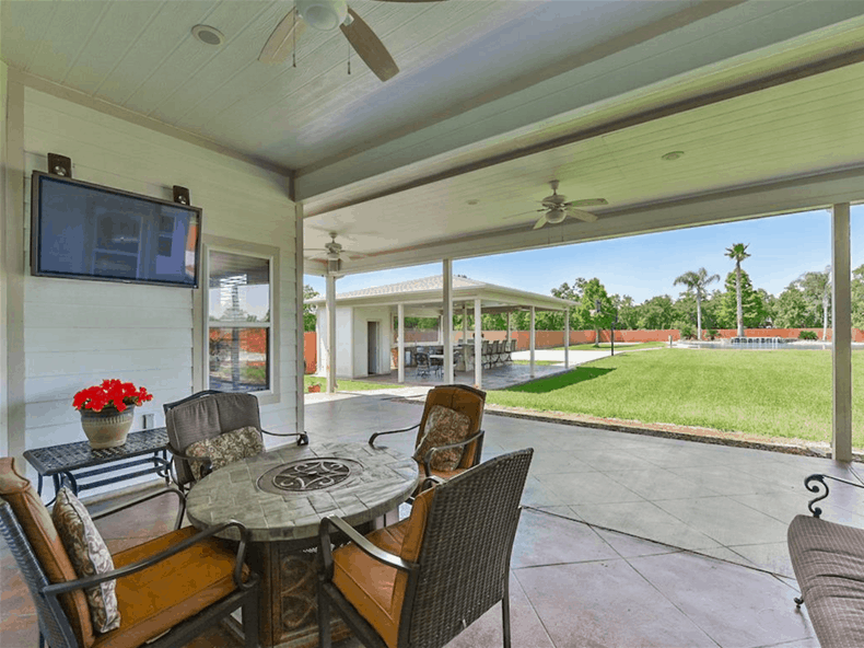 Rear porch with a wall-mounted TV and cushioned chairs surrounding the round table.