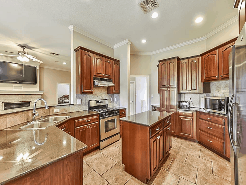 The kitchen is equipped with stainless steel appliances, wooden cabinetry, a center island, and a double bowl sink.