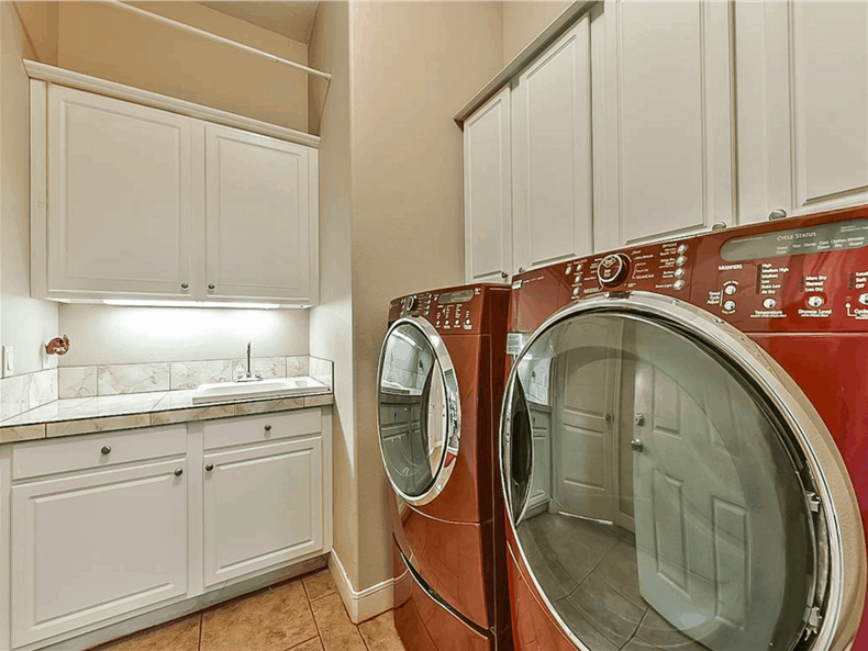 The laundry room offers white cabinets, front load appliances, and a porcelain sink.