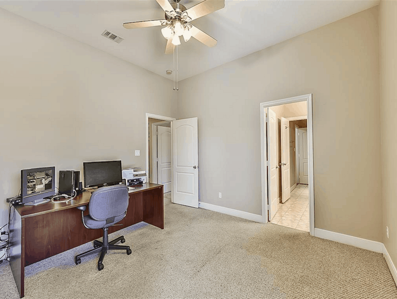Study with a wooden desk and a swivel chair over carpet flooring.