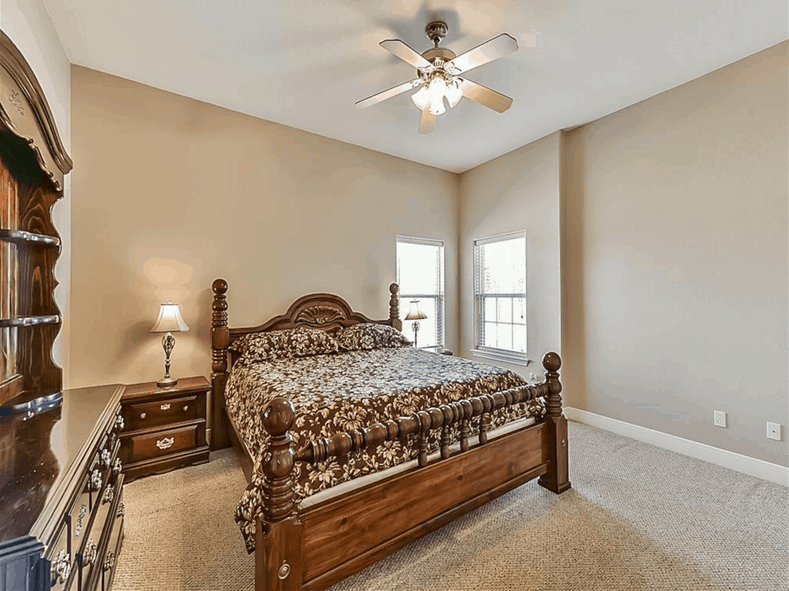This bedroom has a cozy wooden bed, carpet flooring, and a ceiling fan.