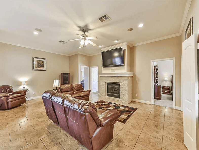 Great room with leather seats and a fireplace topped with a wall-mounted TV.