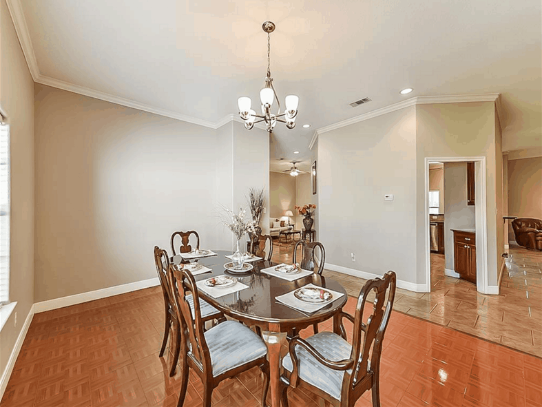 The formal dining room offers cushioned chairs and a round dining table well-lit by a chrome chandelier.