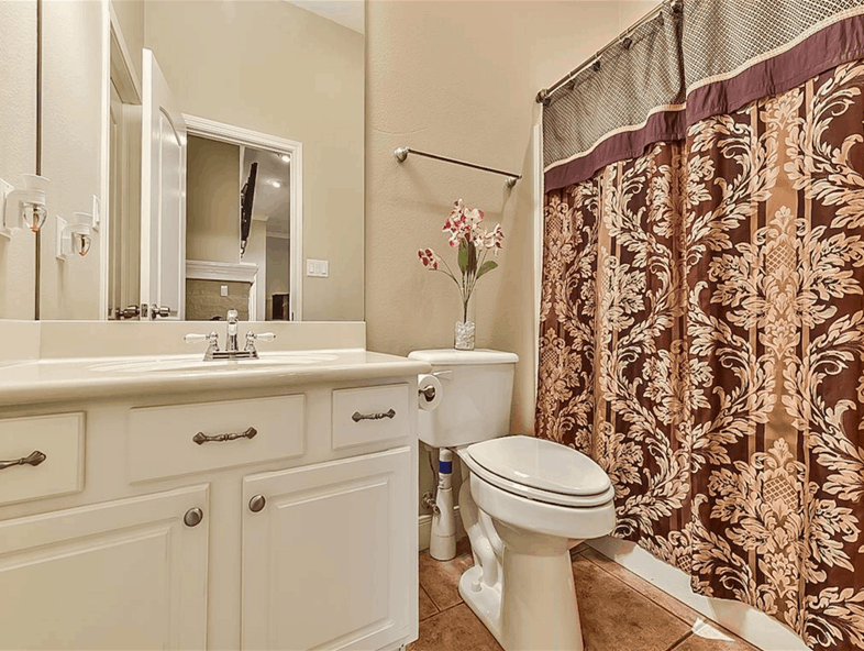 Bathroom equipped with a sink vanity, a toilet, and a tub and shower combo concealed behind the patterned curtain.