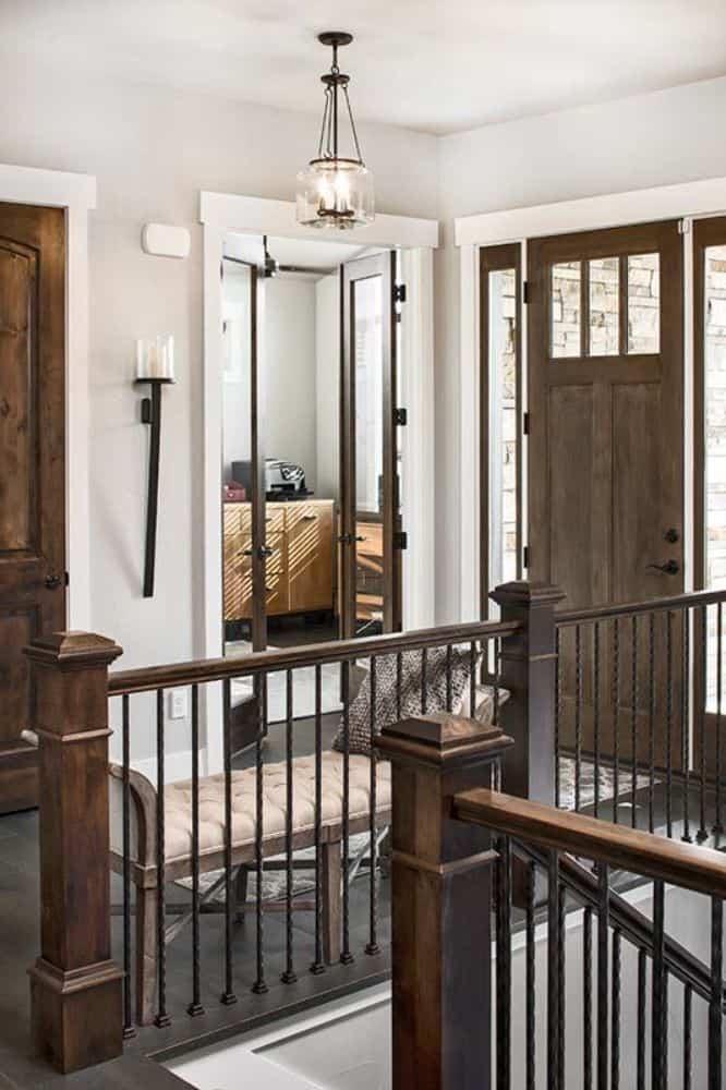 Foyer with a wooden front door, a tufted bench, and wrought iron railings.