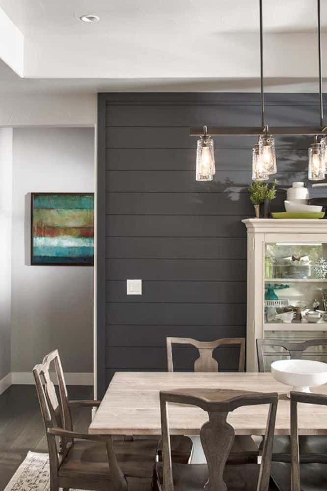 Dining area with a gray paneled accent wall, a white display cabinet, and a wooden dining set illuminated by a glass chandelier.