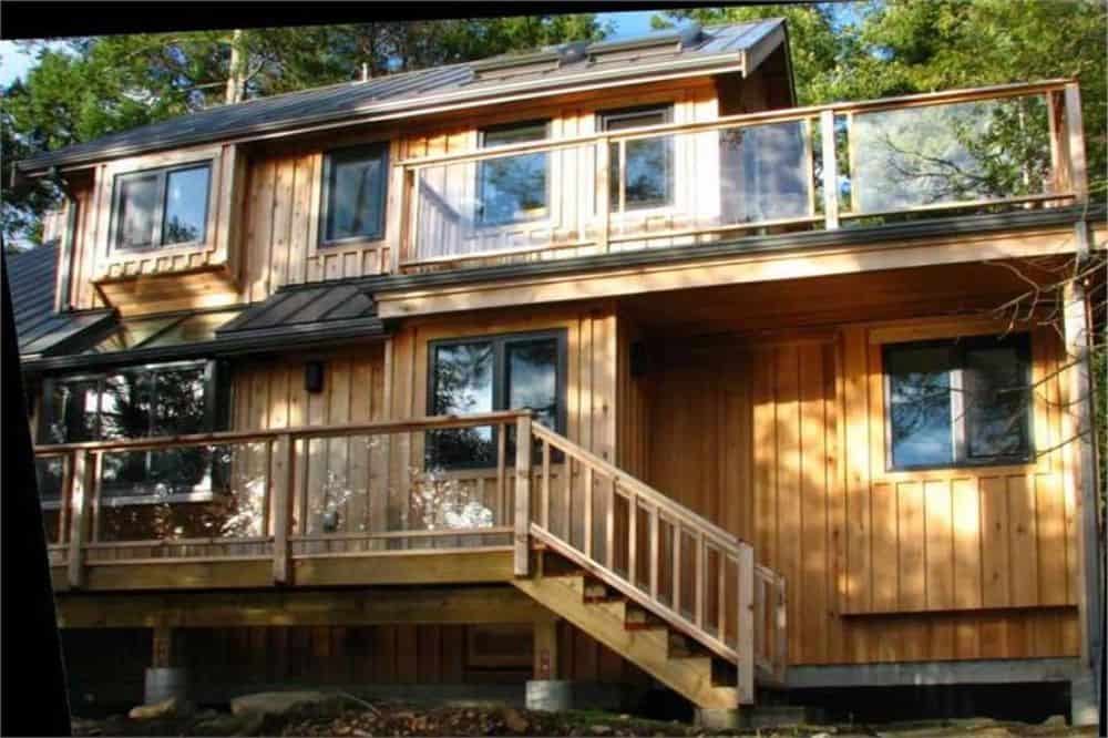 More decks can be seen at the back of the house. They are bordered by glass railings with wooden frames.