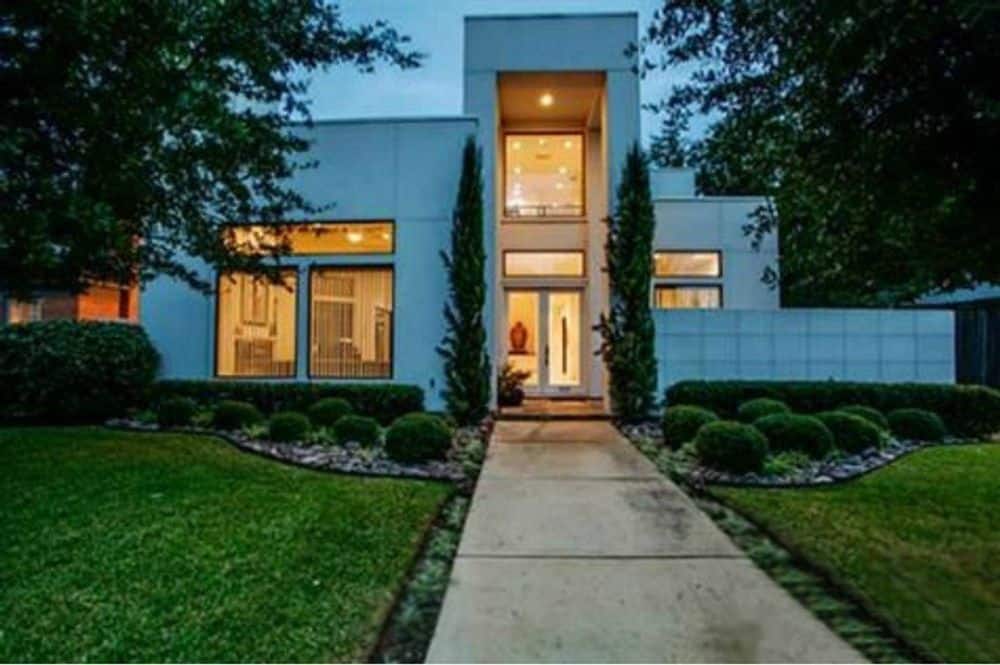 Manicured shrubs and tall pine trees flanking the concrete walkway adorn the two-story contemporary home.