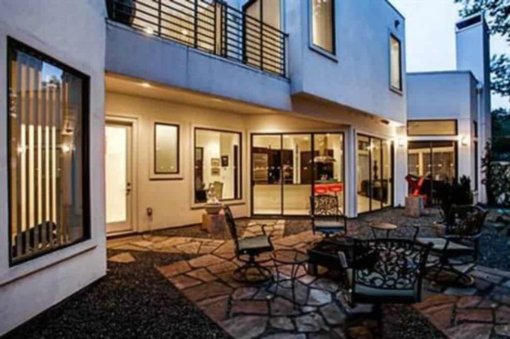 Rear view of the house with an upper balcony and an airy patio furnished with ornate metal chairs.