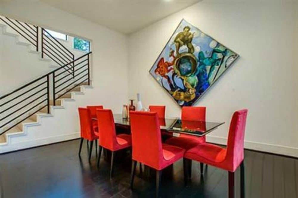 Formal dining room with a glass top dining table, red upholstered chairs, and a bold artwork adorning the beige walls.