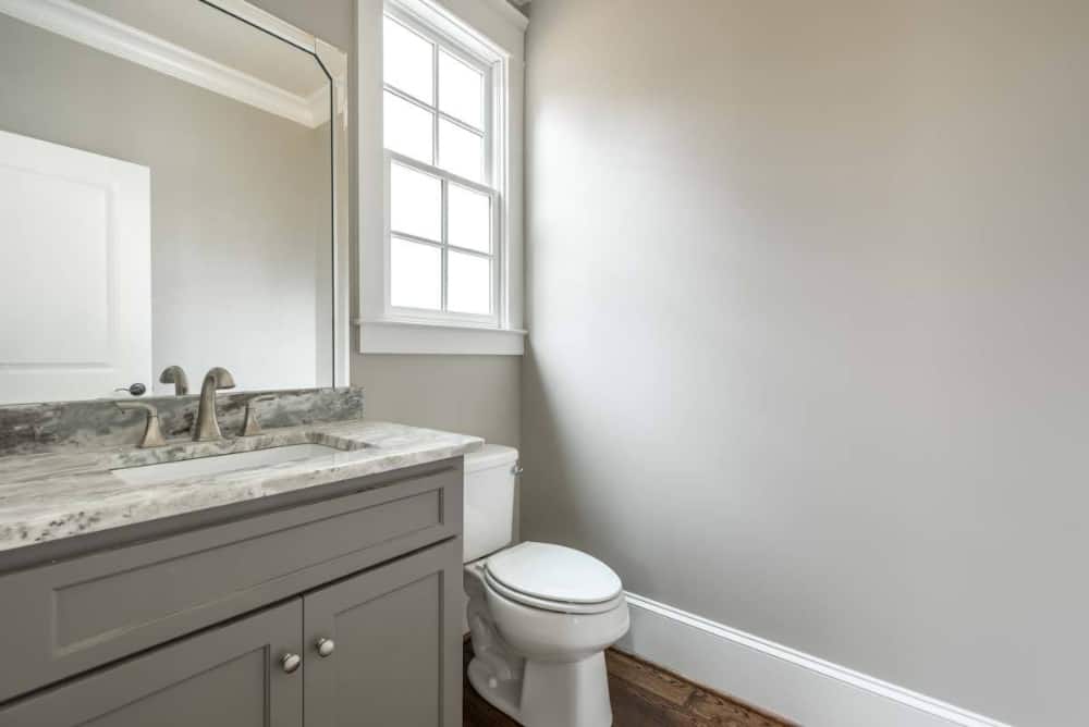 Powder room with a sink vanity, a toilet. and a white framed window.