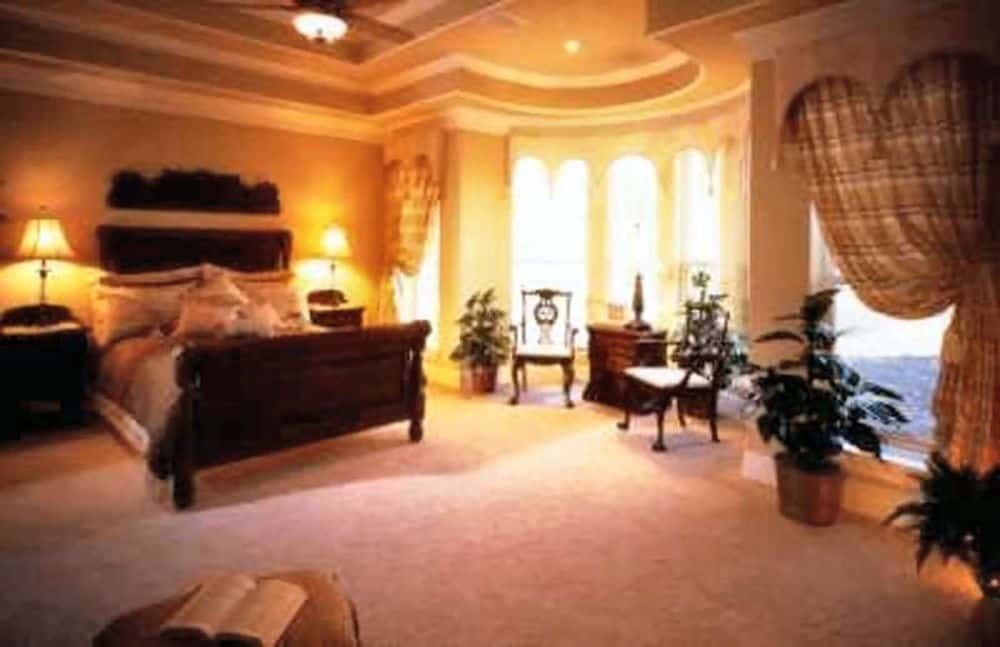 Primary bedroom with a bowed sitting area and dark wood furnishings over carpet flooring.