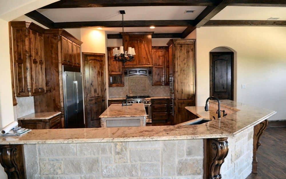 The kitchen is equipped with stainless steel appliances, wooden cabinetry, a center island, and a curved eating bar.
