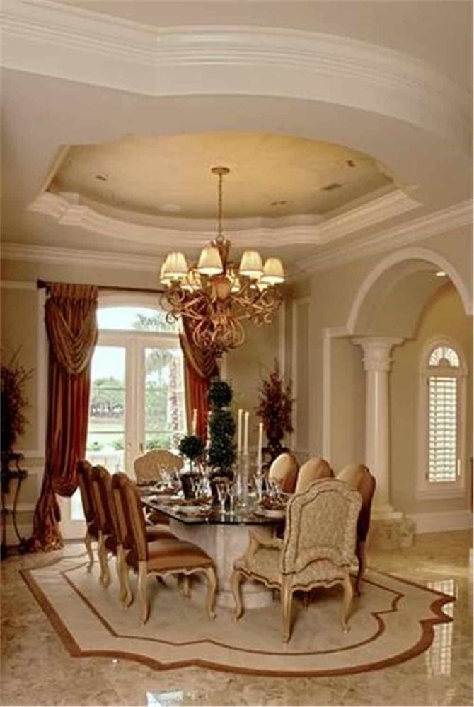 Formal dining room with an ornate chandelier, an 8-seater dining set, and a french door dressed in red draperies.