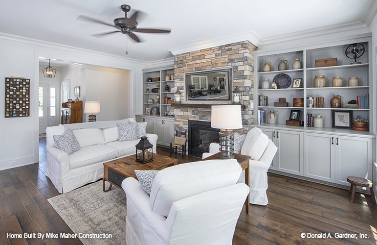 Great room with white seats, a rustic coffee table, and a stone fireplace flanked by built-in cabinets.