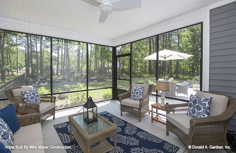 The screened porch offers wicker armchairs and a glass-top coffee table sitting on a blue patterned rug.