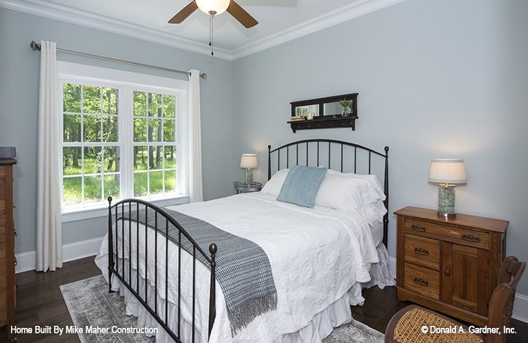 This bedroom has a metal bed, wooden nightstand, and a white framed window that invites natural light in.