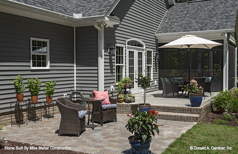Rear patio with plant pedestals and multiple sitting areas over the stone flooring.