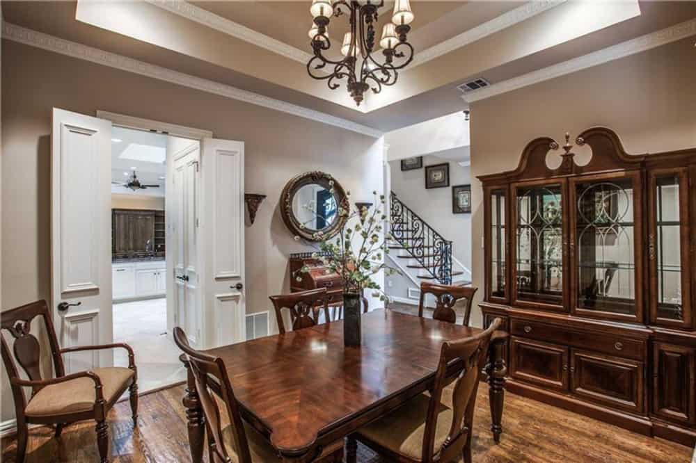 Dining room with wooden dining set, a matching china cabinet, and a wrought iron chandelier mounted on the tray ceiling.