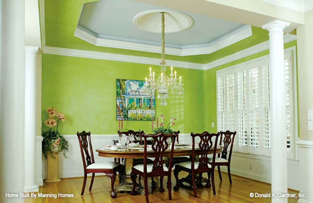 Formal dining room with a round dining set, a crystal chandelier, tray ceiling, and green walls adorned with white wainscoting.