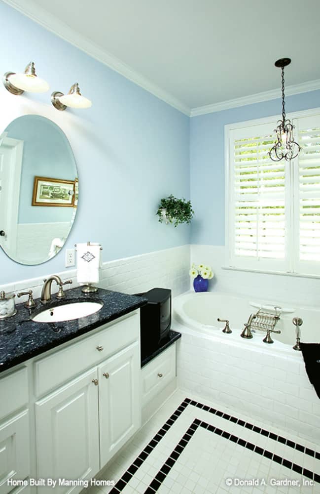 Primary bathroom with light blue walls, tile flooring, and an iron pendant hanging over the bathtub.