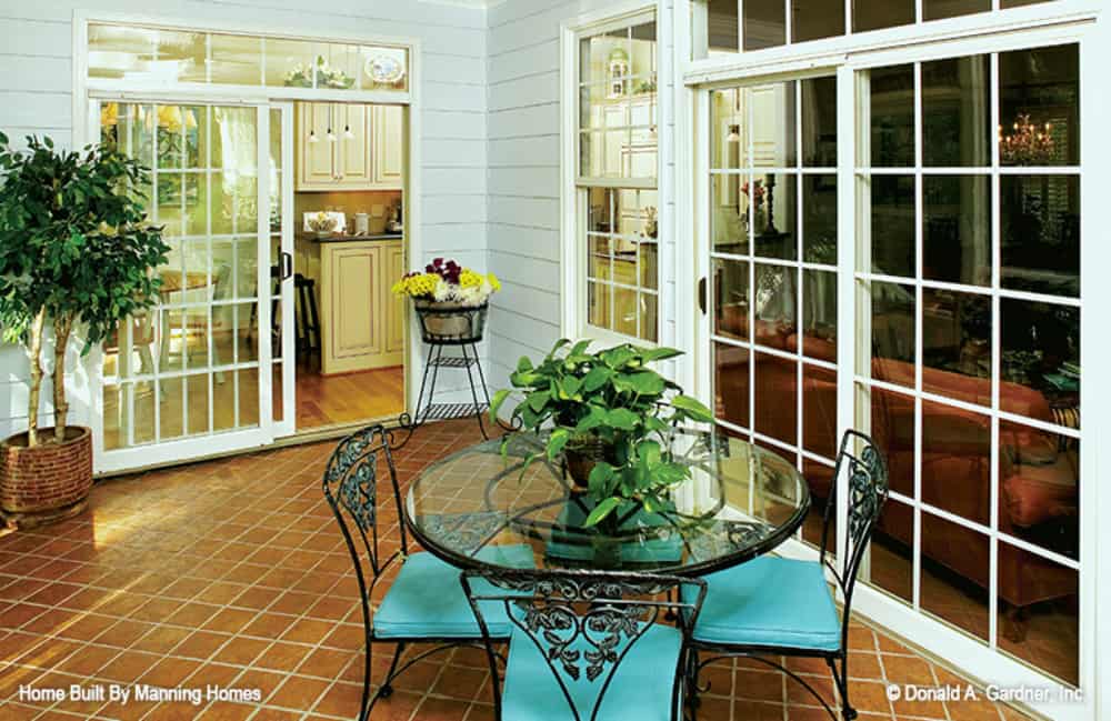 Screened porch with flower pedestal and cushioned chairs surrounding the glass top table.