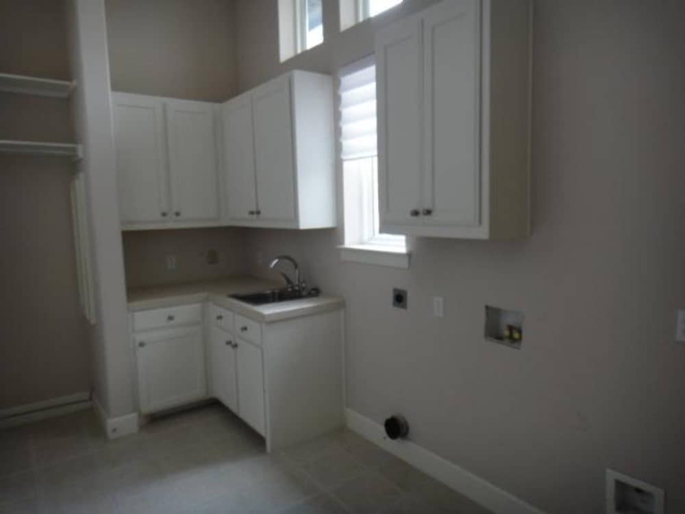 Laundry room with utility sink, white cabinets, and framed windows.
