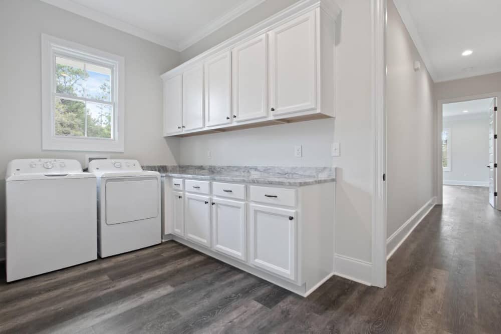 Laundry room with top-load washer and dryer, white cabinets, and marble countertop.