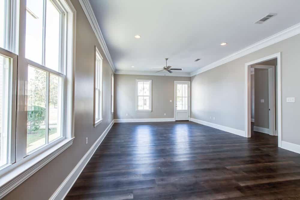 Living room with dark hardwood flooring and beige walls fitted with white framed windows.