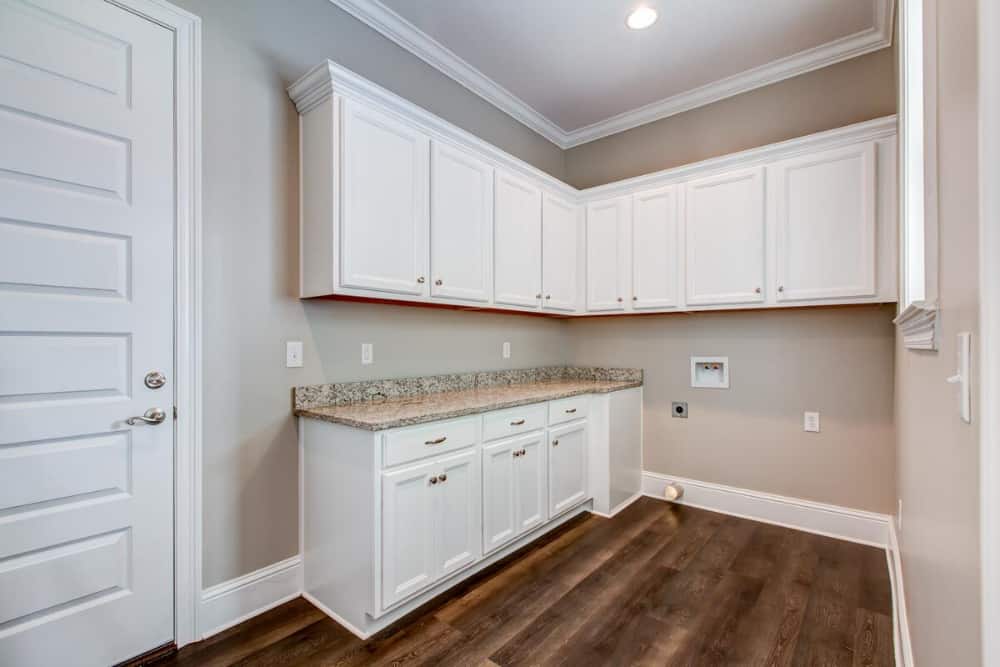 Laundry room with granite countertop and white cabinets fixed against the beige walls.