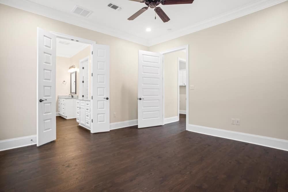 Primary bedroom with dark hardwood flooring, beige walls, and a white double door that opens to the primary bath.