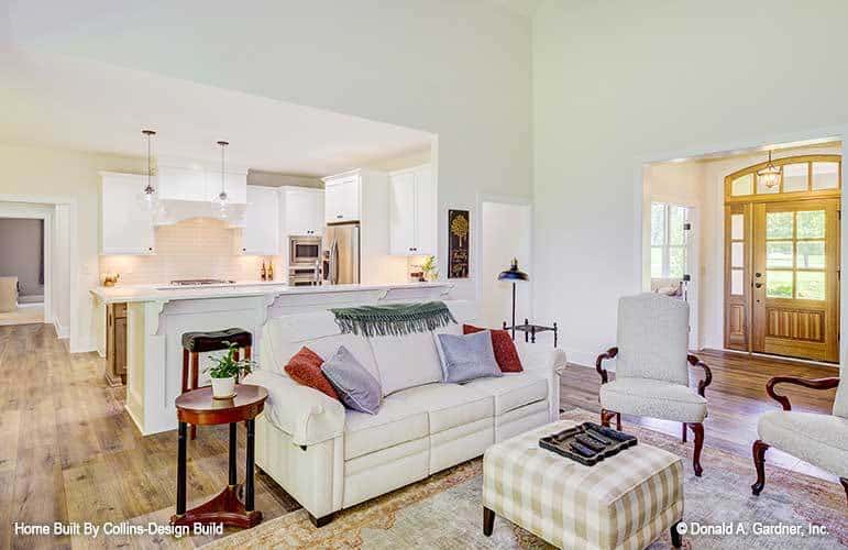 The great room offers beige sectional, upholstered armchairs, and a checkered ottoman over a vintage area rug.