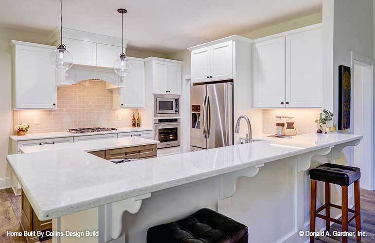 Kitchen with white cabinetry, stainless steel appliances, and a large eating bar paired with tufted stools.